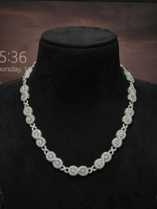 May include: A sparkling silver necklace with a repeating pattern of circular and X-shaped links. The necklace is displayed on a black mannequin, showcasing its intricate design and brilliant shine. The necklace is a statement piece.